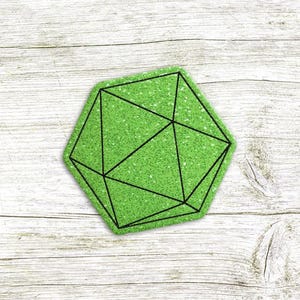 Puede incluir: Un posavasos geométrico verde con un contorno negro de un diseño de poliedro. El posavasos está hecho de un material texturizado y se encuentra sobre una superficie de madera clara.