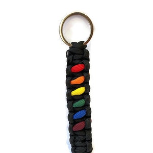 May include: A black paracord keychain with a rainbow colored woven design. The keychain has a silver metal key ring.