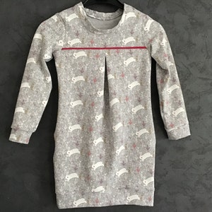 Peut inclure: Une robe grise à manches longues avec un imprimé de lapins blancs et une bande rouge sur la poitrine.