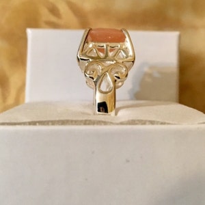 May include: A silver ring with a delicate filigree design and a light pink oval-shaped gemstone.