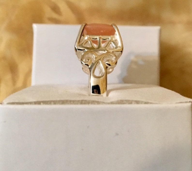 May include: A silver ring with a delicate filigree design and a light pink oval-shaped gemstone.