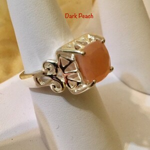 May include: A gold ring with a square, peach-colored gemstone. The ring has a delicate, ornate design.