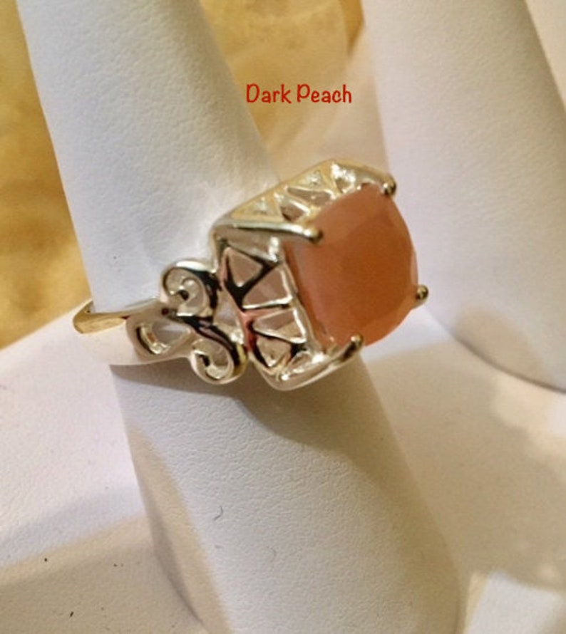 May include: A gold ring with a square, peach-colored gemstone. The ring has a delicate, ornate design.