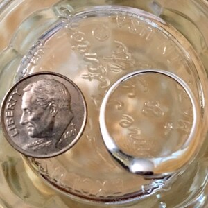 May include: A silver ring and a US dime coin with the inscription "LIBERTY" are sitting in a clear glass jar filled with water.