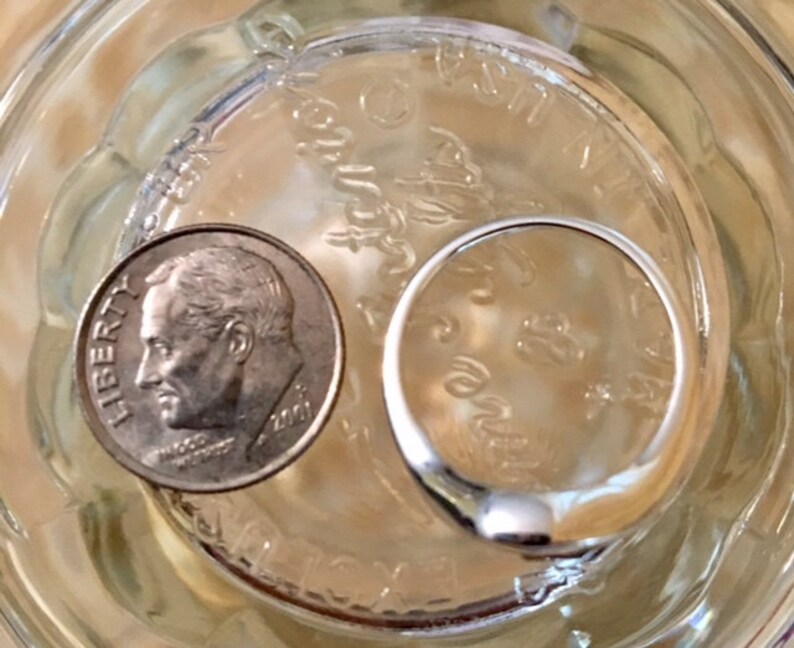 May include: A silver ring and a US dime coin with the inscription "LIBERTY" are sitting in a clear glass jar filled with water.