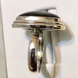 Op de afbeelding: Een zilveren ring met een zwarte ovale edelsteen gezet in een dubbele rand bezel. De ring heeft een eenvoudige band.