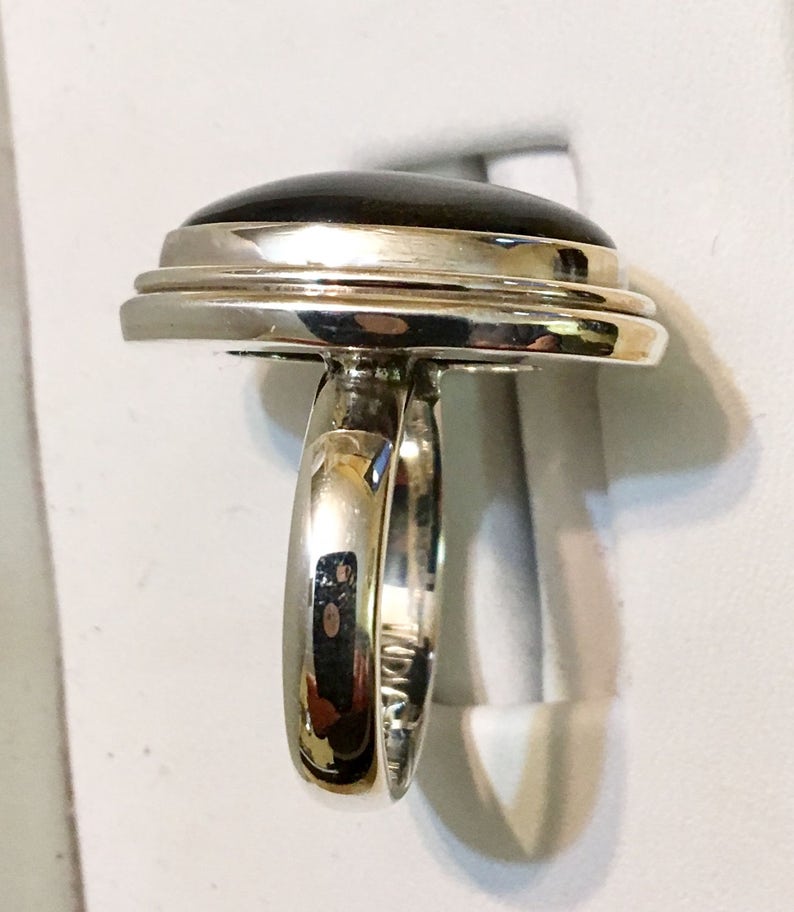 Op de afbeelding: Een zilveren ring met een zwarte ovale edelsteen gezet in een dubbele rand bezel. De ring heeft een eenvoudige band.