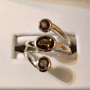 Peut inclure: Une bague en argent avec trois pierres pr&eacute;cieuses brunes serties dans la bande. La bague est con&ccedil;ue avec trois griffes qui s'enroulent autour du doigt.