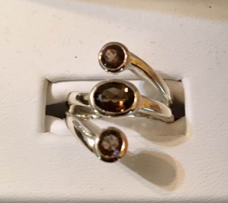 Peut inclure: Une bague en argent avec trois pierres pr&eacute;cieuses brunes serties dans la bande. La bague est con&ccedil;ue avec trois griffes qui s'enroulent autour du doigt.