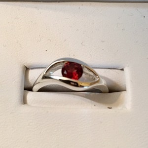 May include: A silver ring with a red gemstone set in a wave-like band.