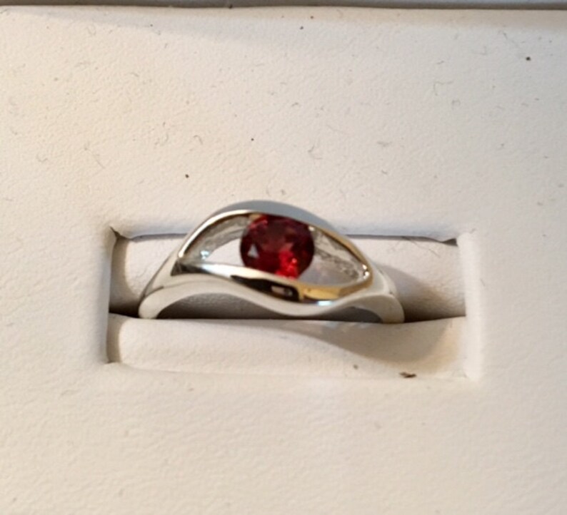 May include: A silver ring with a red gemstone set in a wave-like band.