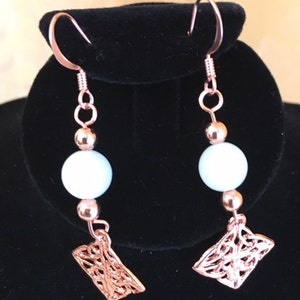 May include: Rose gold earrings with white beads and a filigree design.