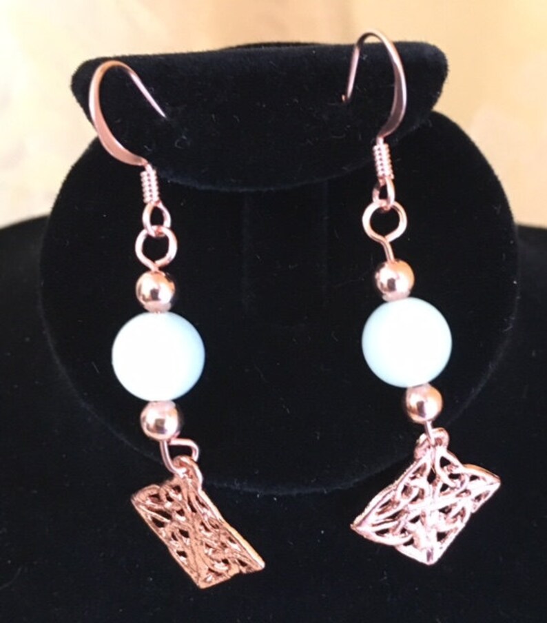 May include: Rose gold earrings with white beads and a filigree design.
