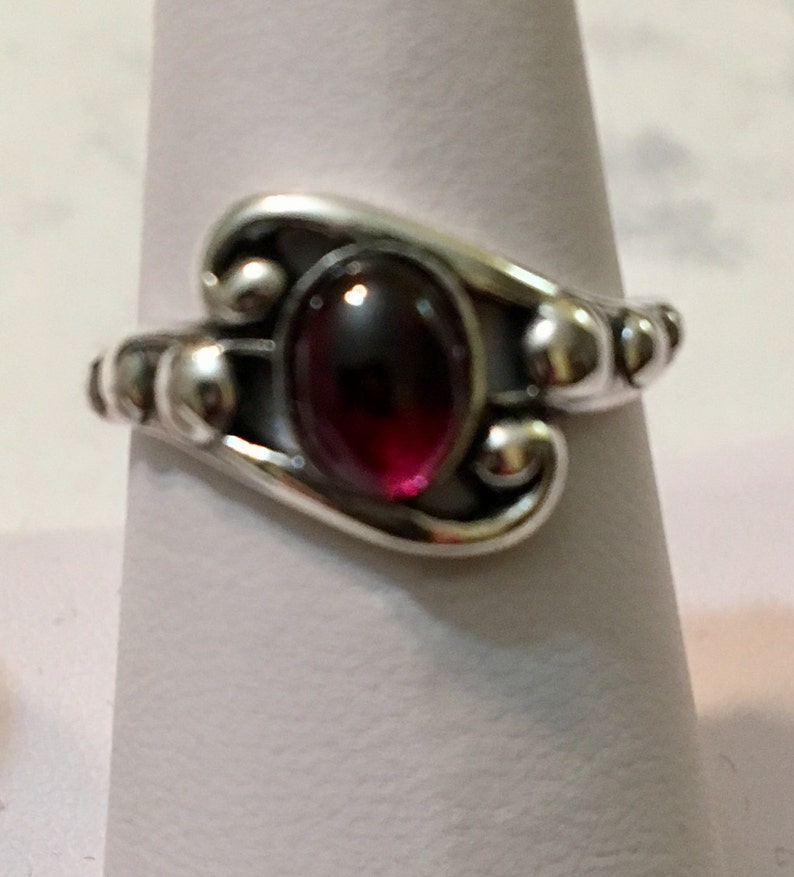 May include: A silver ring featuring a dark red gemstone set in a swirling design.