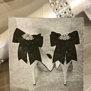 K&ouml;nnte beinhalten: Ein Paar schwarze Satin-Schuhe mit Strass-Verzierungen. Die Schuhe haben einen hohen Absatz und eine spitze Zehenpartie.