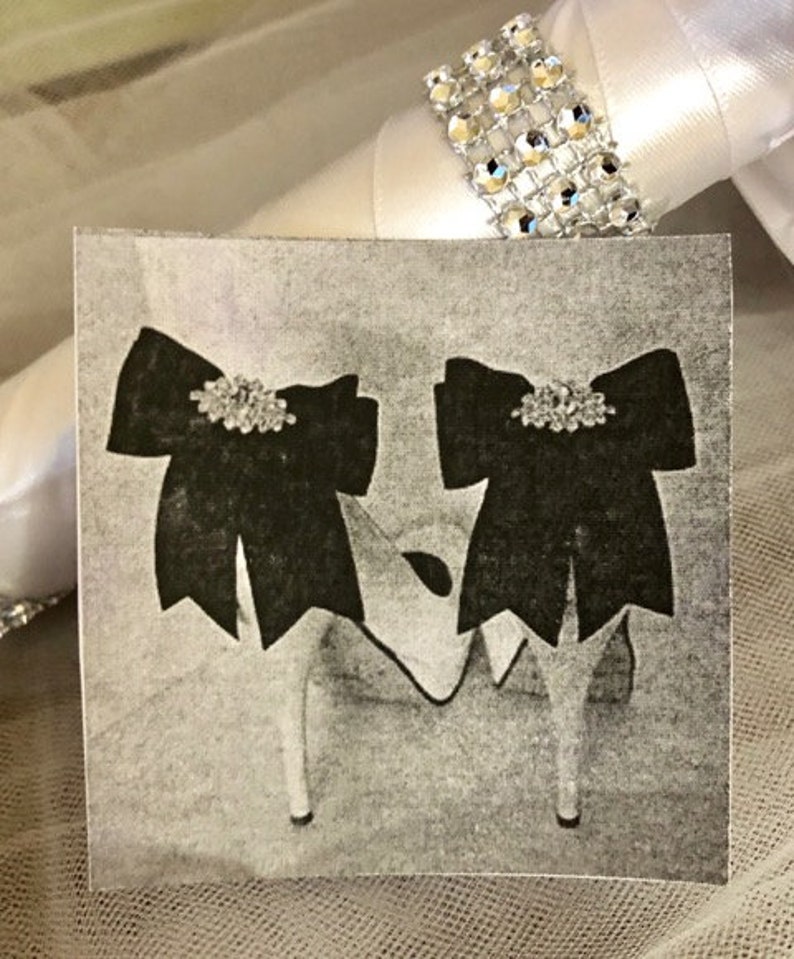 K&ouml;nnte beinhalten: Ein Paar schwarze Satin-Schuhe mit Strass-Verzierungen. Die Schuhe haben einen hohen Absatz und eine spitze Zehenpartie.