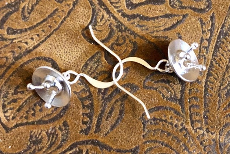 May include: A pair of silver earrings with a circular design. The earrings have a simple, elegant style.