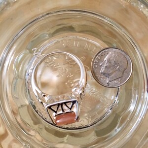 May include: A silver ring with a pink stone set in a geometric design. The ring is next to a US dime coin.