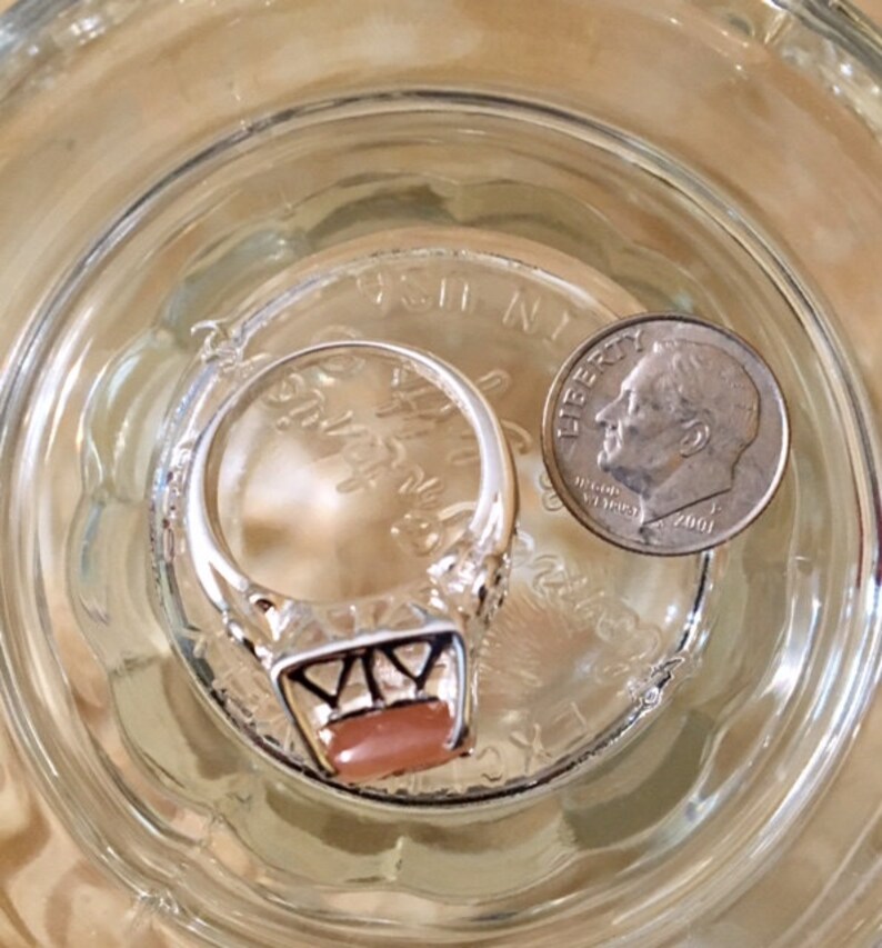 May include: A silver ring with a pink stone set in a geometric design. The ring is next to a US dime coin.