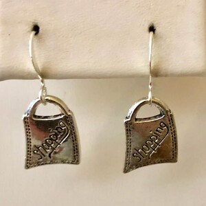 May include: Silver shopping bag earrings with a textured finish and the word "Shopping" engraved on each bag.