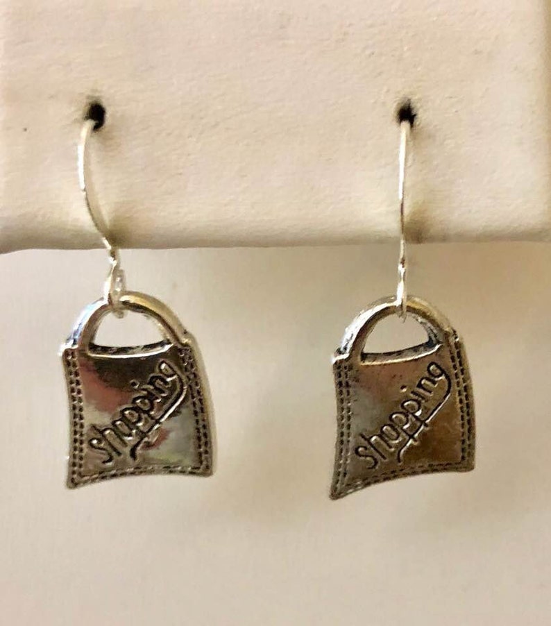 May include: Silver shopping bag earrings with a textured finish and the word "Shopping" engraved on each bag.