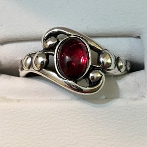 May include: A silver ring featuring a red oval gemstone set in a decorative swirl design.