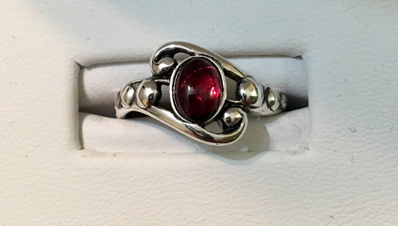 May include: A silver ring featuring a red oval gemstone set in a decorative swirl design.