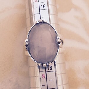 May include: A silver ring with a light purple oval gemstone. The ring is on a ring sizer, showing a size 18.