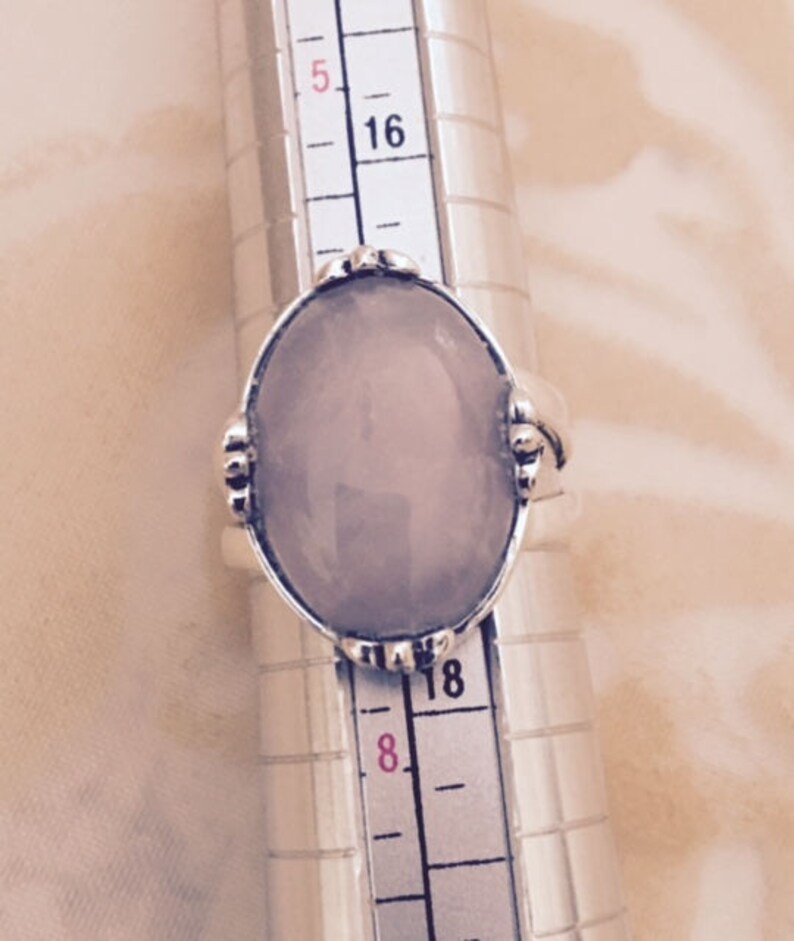 May include: A silver ring with a light purple oval gemstone. The ring is on a ring sizer, showing a size 18.