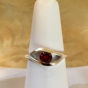 May include: A silver ring with a red gemstone set in a unique eye-shaped design.