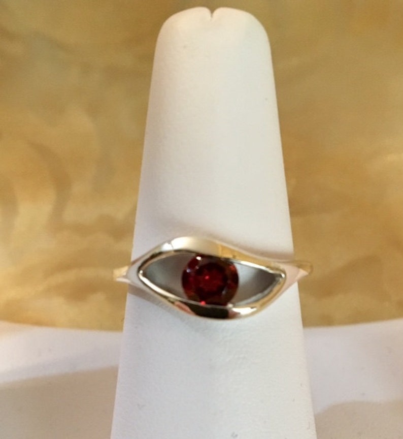 May include: A silver ring with a red gemstone set in a unique eye-shaped design.