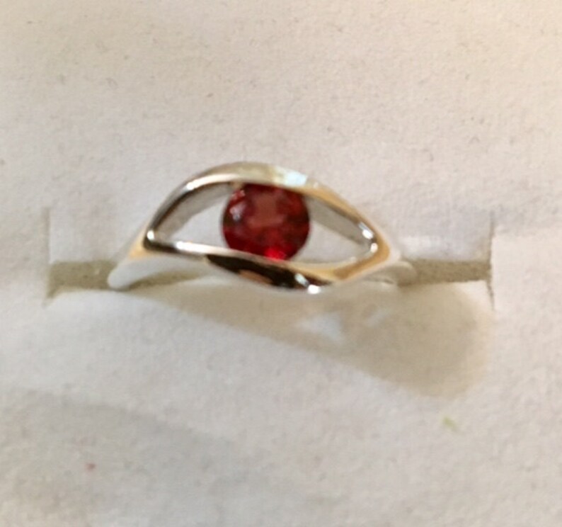 May include: A silver ring with a red gemstone set in a unique eye-shaped design.
