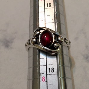 May include: A silver ring with a red gemstone and a beaded band. The ring is size 18.