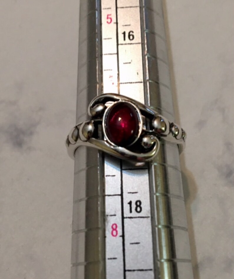 May include: A silver ring with a red gemstone and a beaded band. The ring is size 18.