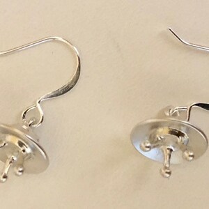 May include: A pair of silver earring findings with a small, round, flat base and three prongs. The findings have a hook closure.
