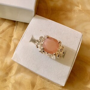 May include: A silver ring with a large, light pink gemstone set in a detailed, ornate design.