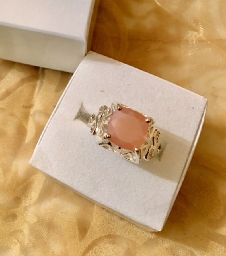 May include: A silver ring with a large, light pink gemstone set in a detailed, ornate design.