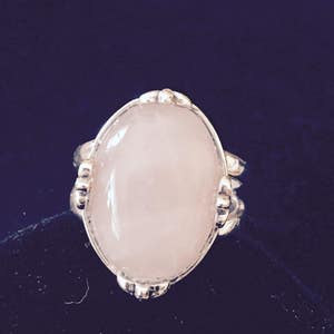 May include: A silver ring with a large oval-shaped rose quartz gemstone.