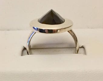 May include: A silver ring with a black gemstone set in a circular bezel. The ring is on a white background.