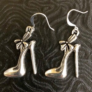 K&ouml;nnte beinhalten: Ein Paar silberne Ohrringe in Form von Schuhen mit hohen Abs&auml;tzen und einer Schleife.