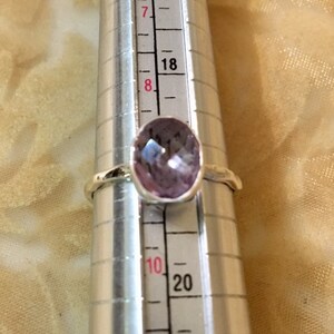 Pu&ograve; includere: Un anello d'argento con una pietra preziosa di colore viola chiaro. L'anello &egrave; su uno strumento di misurazione e la dimensione &egrave; 8.
