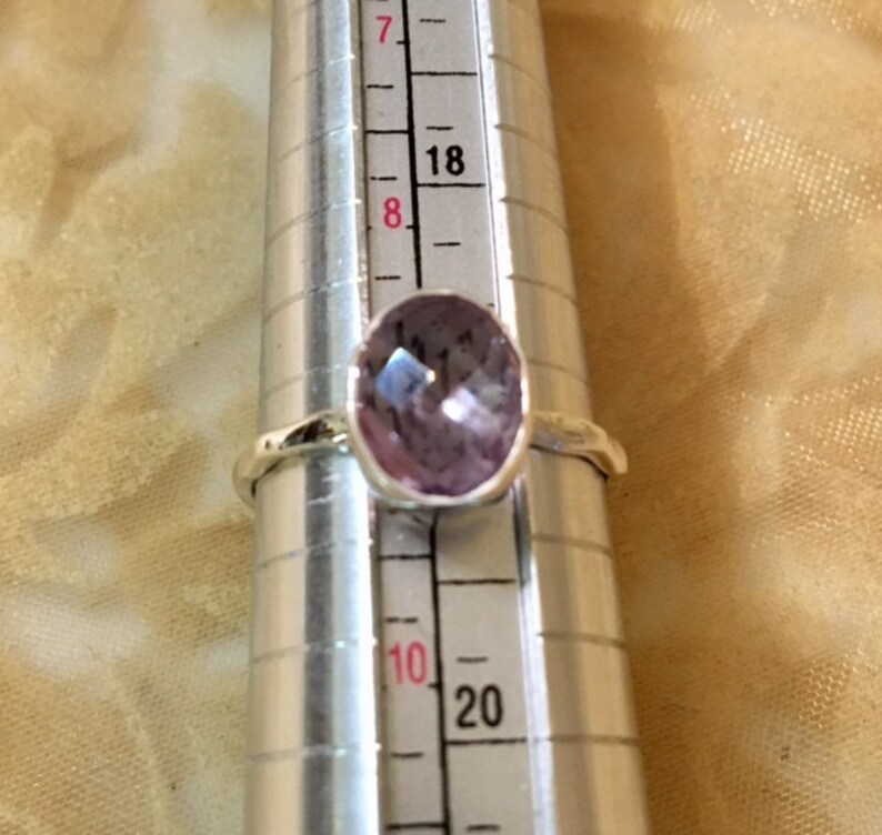 Pu&ograve; includere: Un anello d'argento con una pietra preziosa di colore viola chiaro. L'anello &egrave; su uno strumento di misurazione e la dimensione &egrave; 8.