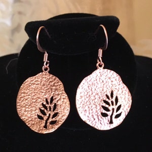 May include: A pair of copper earrings with a textured finish and a cut-out tree design.