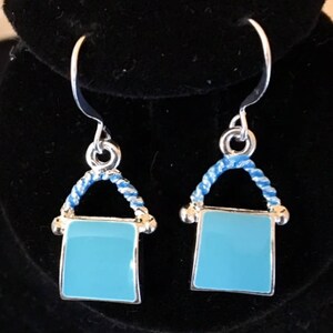 Pu&ograve; includere: Un paio di orecchini pendenti in argento con un quadrato in smalto blu e un design a corda blu e bianca.