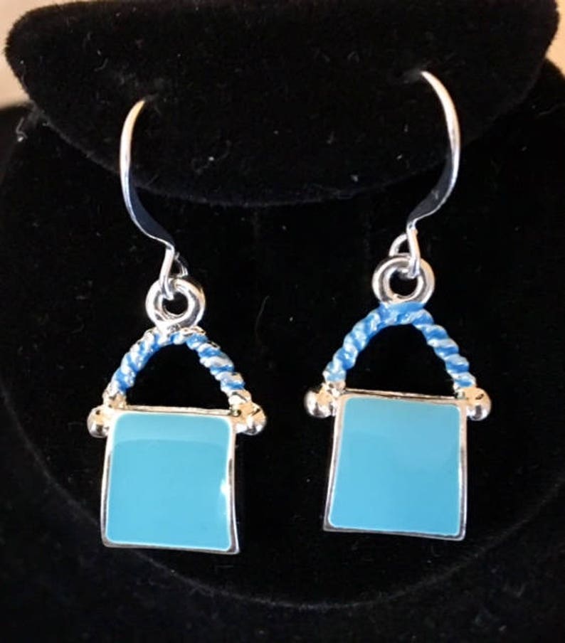 Pu&ograve; includere: Un paio di orecchini pendenti in argento con un quadrato in smalto blu e un design a corda blu e bianca.