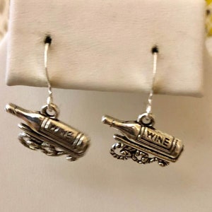 May include: Silver earrings with a wine bottle charm. The bottle charm has the word "wine" on it.