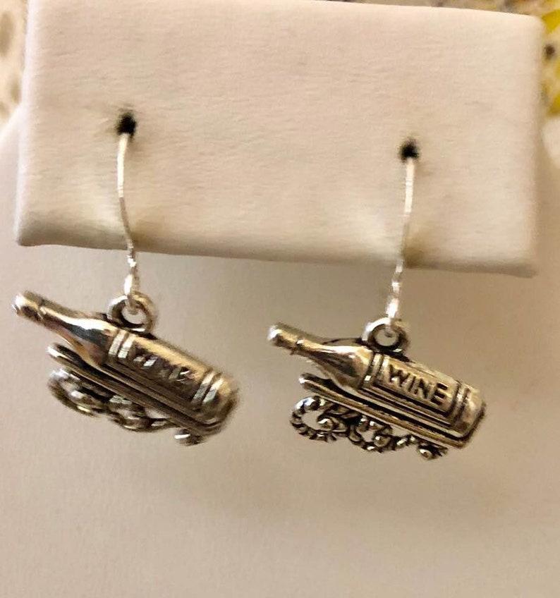 May include: Silver earrings with a wine bottle charm. The bottle charm has the word "wine" on it.