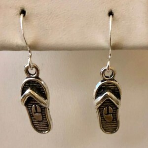 May include: A pair of silver dangle earrings featuring a flip-flop design.