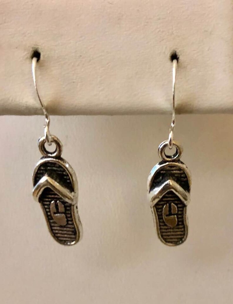 May include: A pair of silver dangle earrings featuring a flip-flop design.