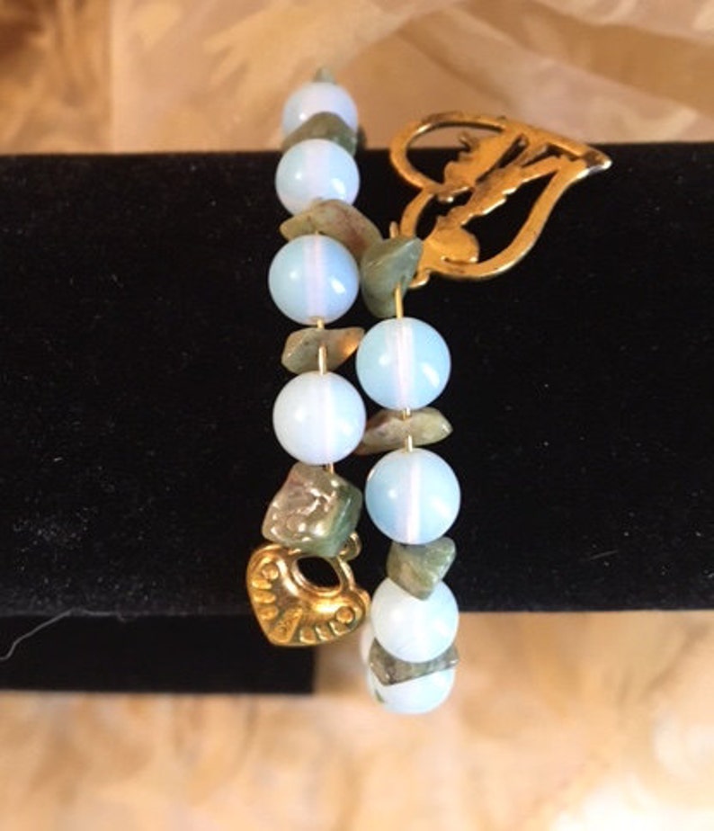 May include: Two bracelets with light blue and green beads and gold heart charms.